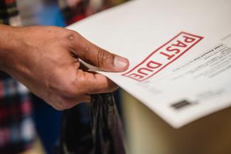 Hand holding a bill with a red "Past Due" stamp on it